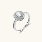 Sterling silver ring with oval moissanite center stone surrounded by double halo of sparkling stones on neutral background.