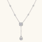 Sterling silver necklace with cushion-cut moissanite in halo setting and teardrop pendant, displayed on cream background.