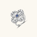 Flower-shaped sterling silver ring with brilliant round moissanite center stone and crystal petals on neutral background