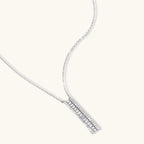 White gold plated necklace with vertical cubic zirconia pendant and matching hoop earrings on neutral background