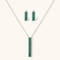 White gold plated jewelry set with emerald green rectangular stones and clear crystals in geometric rows on white background.