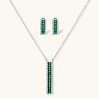 White gold plated jewelry set with emerald green rectangular stones and clear crystals in geometric rows on white background.