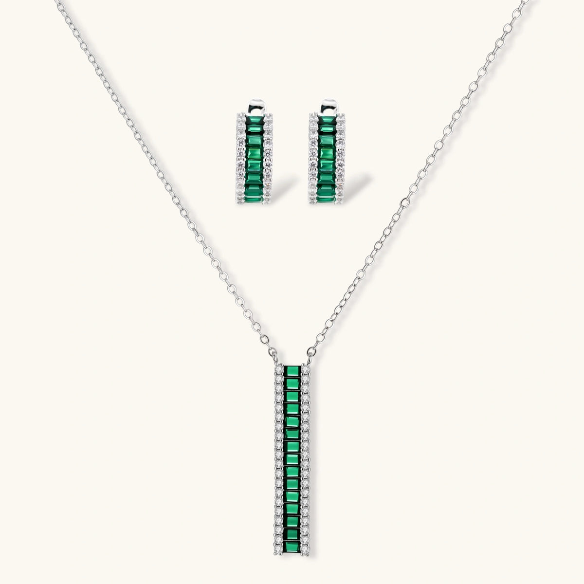 White gold plated jewelry set with emerald green rectangular stones and clear crystals in geometric rows on white background.