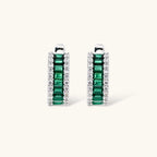 White gold plated jewelry set with emerald green rectangular stones and clear crystals in geometric rows on white background.