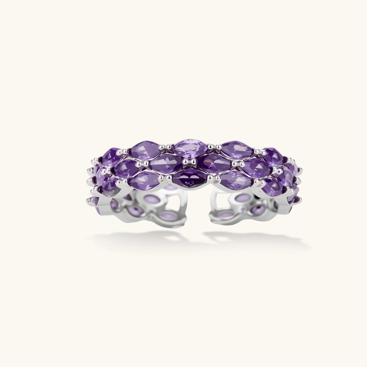 Close-up of adjustable ring with oval purple zirconia stones in white gold-plated copper setting on neutral background.