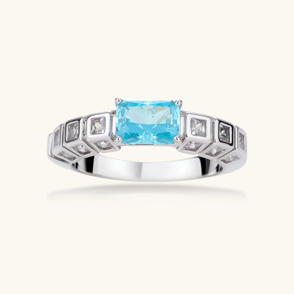 Geometric silver-plated ring with rectangular aqua cubic zirconia center and square crystal details on adjustable band.