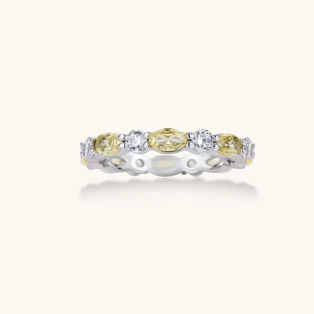 Platinum-plated copper ring with alternating clear and pale yellow oval stones in an eternity band design on white background.